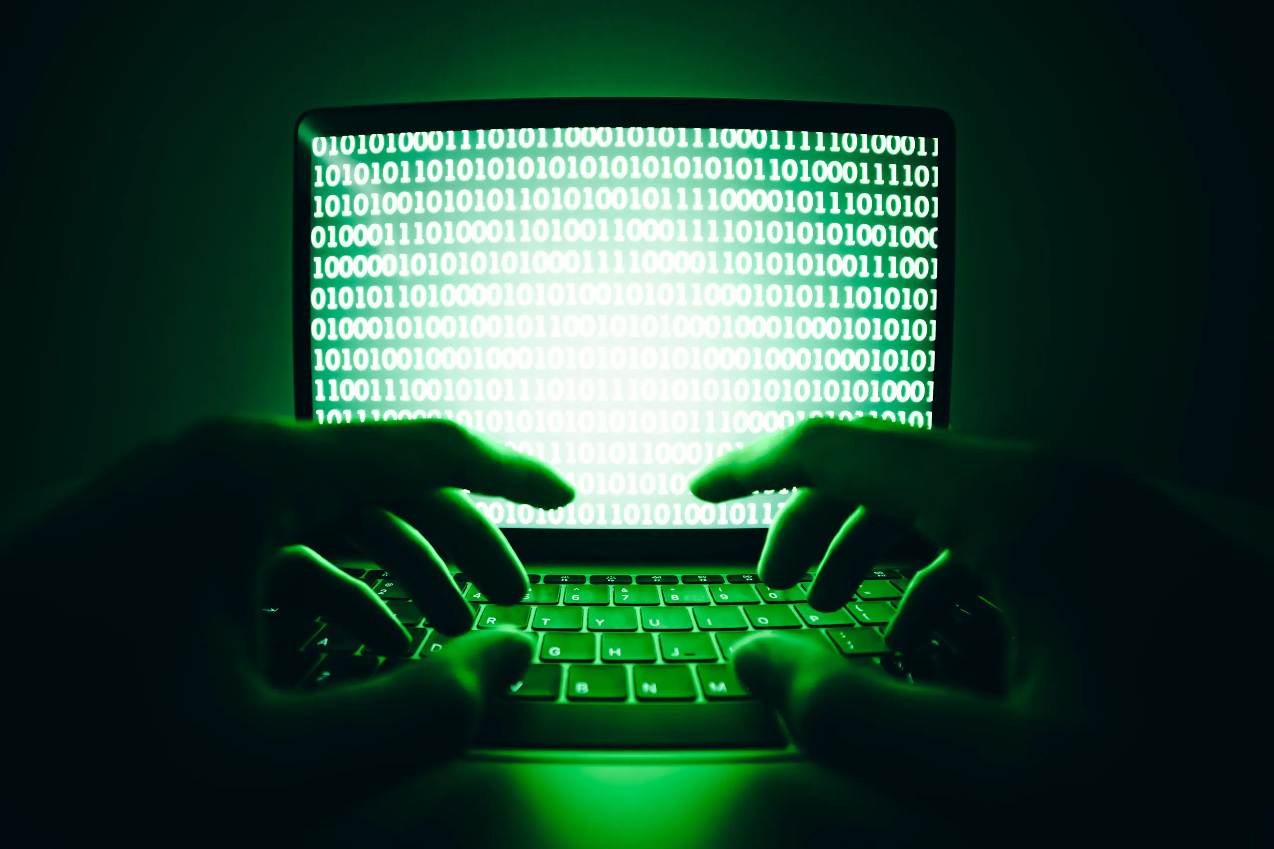 Hacker typing code on a laptop in a dark room